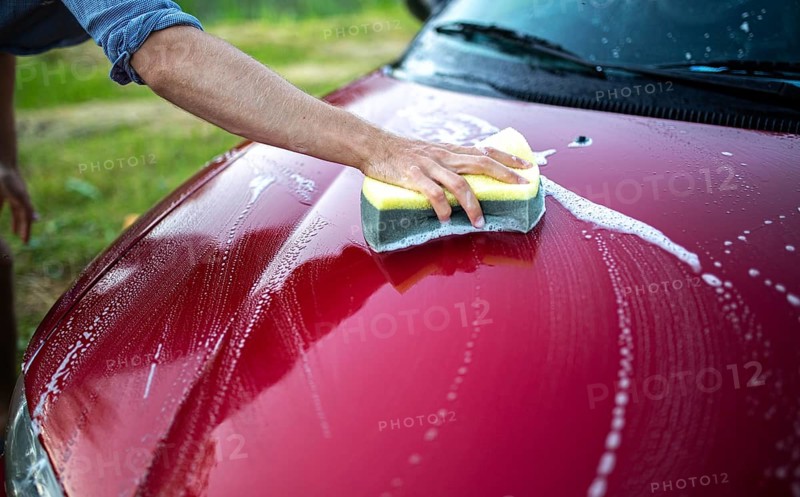 Close-up of a hand washing the hood of a red car with a sponge and soap