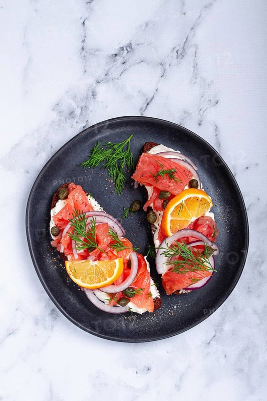 Sandwich with freshly smoked salmon, on black bread, with cottage cheese, with herbs and red onions, capers and pieces of citrus fruits, on a marble countertop, breakfast, no people