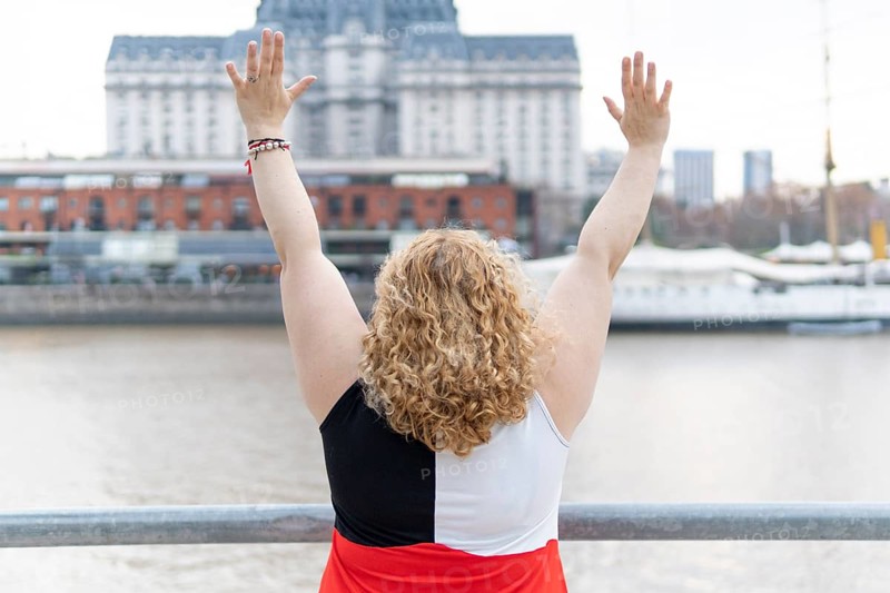 Plus size blonde woman on her back standing on the waterfront with her arms outstretched celebrating