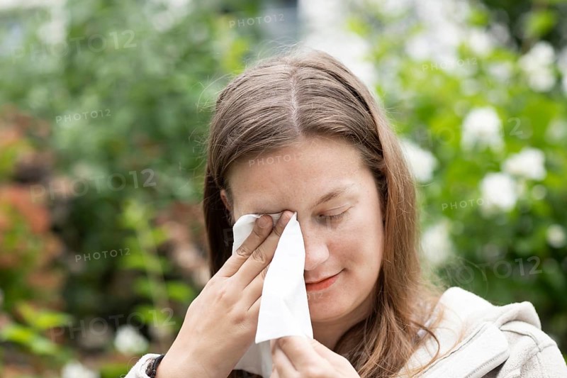 Young woman suffers from hay fever and uses a paper handkerchief outdoors, Freiburg, Baden-Württemberg, Germany, Europe