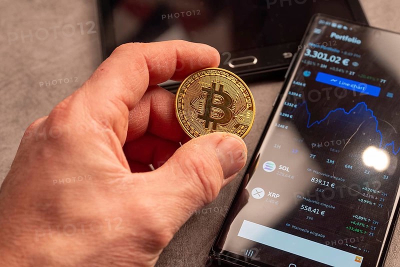 A hand shows a Bitcoin coin next to a smartphone with portfolio data