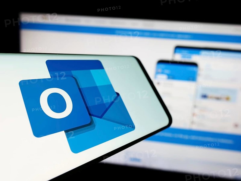 Stuttgart, Germany, 09-21-2023: Mobile phone with logo of email software Microsoft Outlook on screen in front of company website. Focus on center-left of phone display, Europe