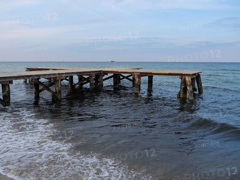 An old wooden jetty juts into the sea, surrounded by gentle waves under an evening sky, sopot, baltic sea, poland