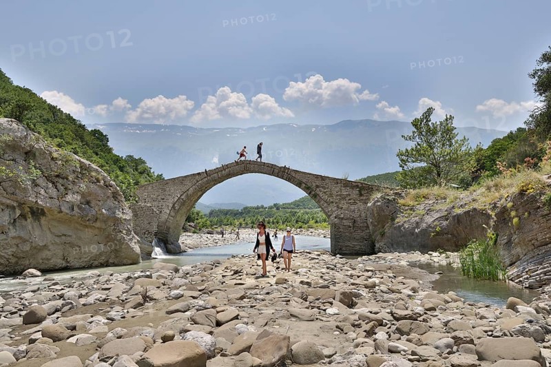 Two young woman walking barefoot in the riverbed over large stones, Ottoman stone bridge, Kadiut Bridge, Lengarica Canyon, Benje, Albania, Europe