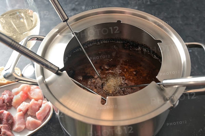 View into a fondue pot with boiling hot oil, long forks, pieces of meat and wine, festive dinner for parties with friends and family, selected focus, narrow depth of field