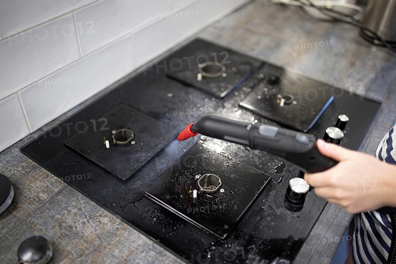 Focused steam cleaning of a black stovetop area in the kitchen