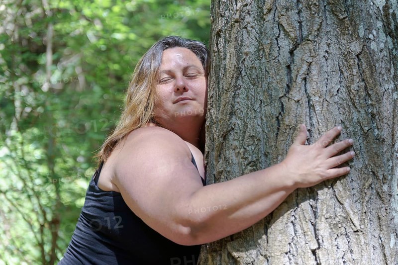 Contented young woman hugging a large tree with a blissful expression and her eyes closed in a concept of save the forest, stop deforestation, earth's day, connecting with nature