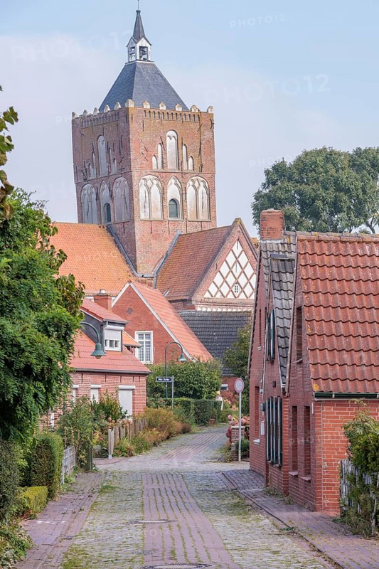 Historic village street with brick houses and a large tower in the background, krummhörn, east frisia, germany