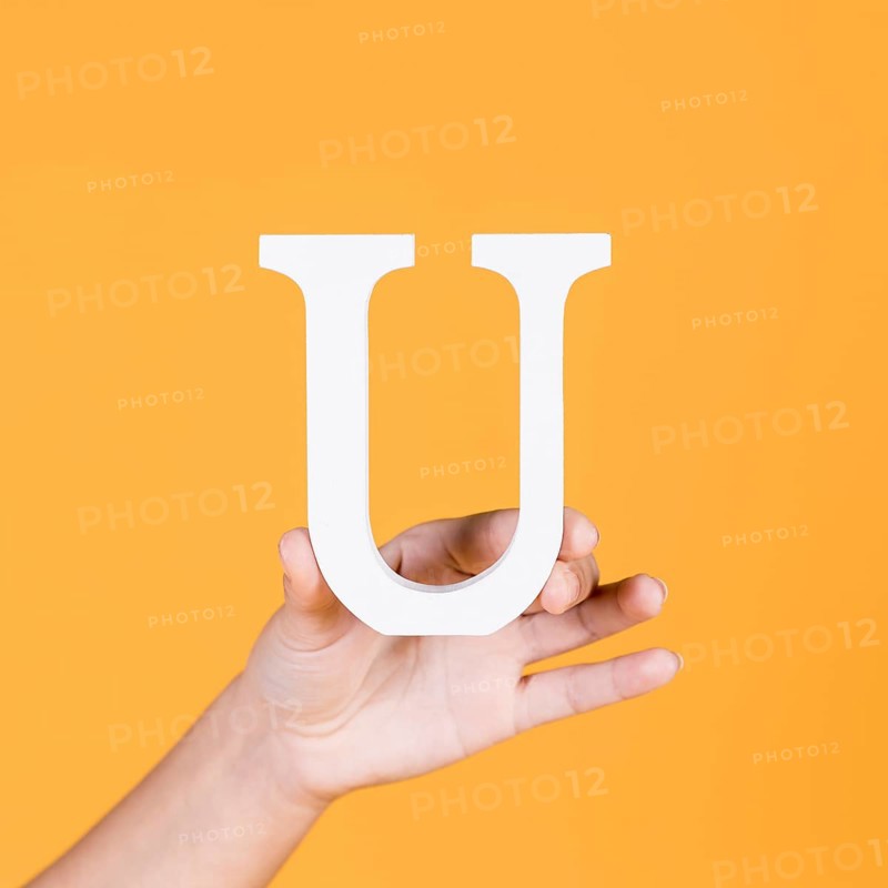 Female hand holding white uppercase alphabet u yellow surface