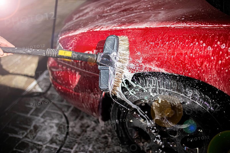 Washing a soapy red car focusing on the side and tire with a brush