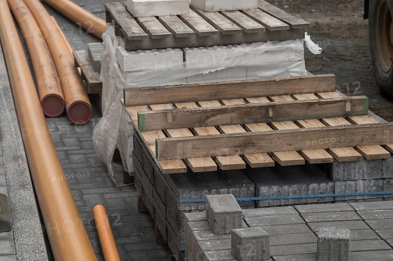Construction materials including paving stones, orange pipes and wooden pallets laying on a cobblestone street during roadworks
