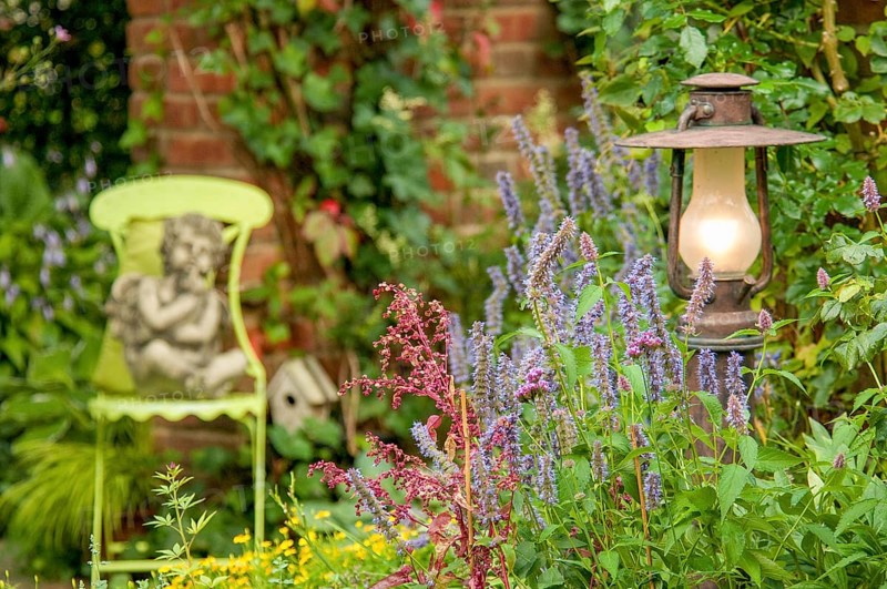 A garden with a statue of an angel on a green chair, surrounded by flowering plants and a burning lamp, Borken, münsterland, germany