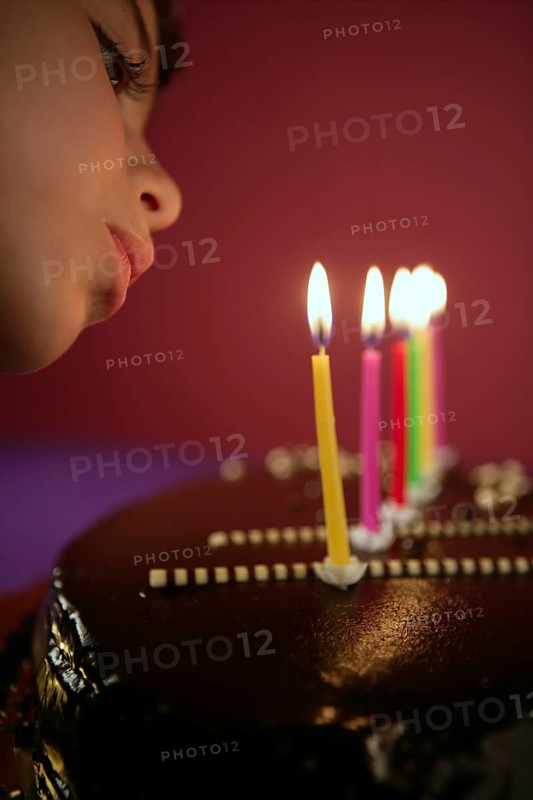 Little girl blowing birthday chocolate cake candles in a row over red background