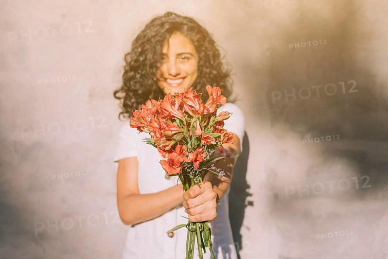 Young woman standing against wall holding (alstroemeria) red flower bouquet hands