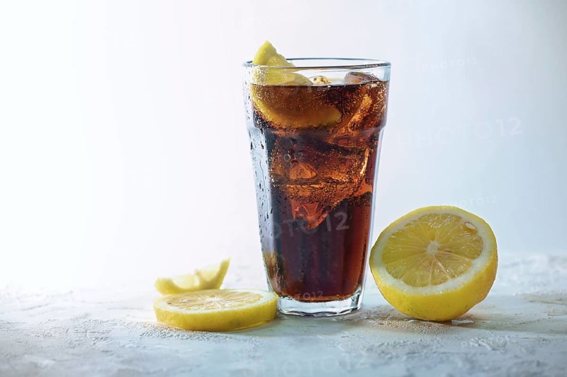 Fresh cola with ice cubes and lemon slices in a drinking glass against a light blue gray background, refreshing sweet caffeine drink, copy space, selected focus, narrow depth of field