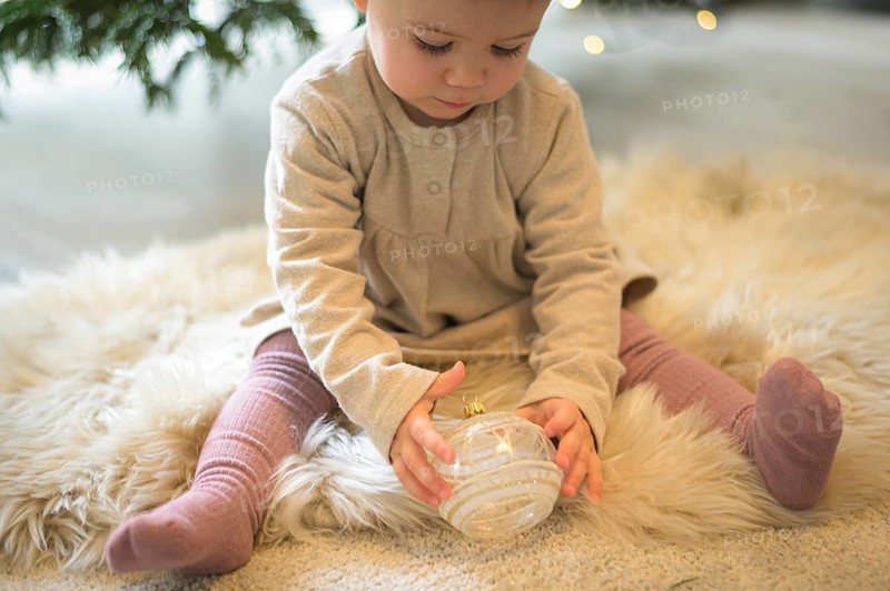 Toddler sitting on a rug and looking at a Christmas tree bauble in a cosy setting