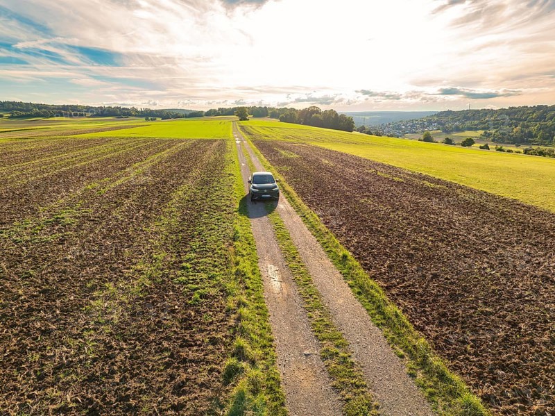Black car driving on a long, straight country lane through scenic fields under a cloudy sky, car sharing, VW ID5, Calw, Black Forest, Germany, Europe