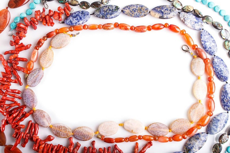 Frame of semiprecious stone beads on white background, top view