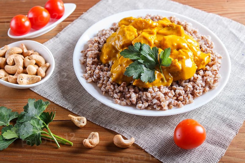 Buckwheat with chicken curry sauce with cashew on brown wooden background. close up