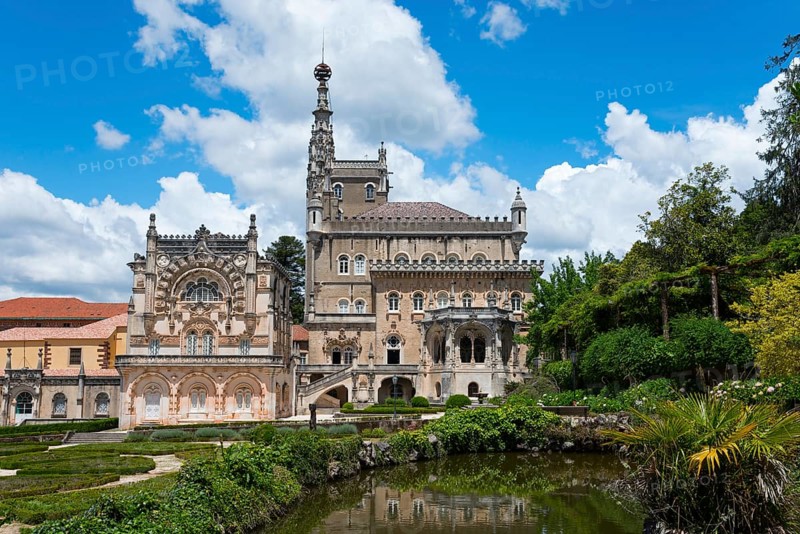 Ein prächtiges Schloss mit aufwendiger Architektur und Türmen vor einem blauen Himmel mit Wolken, umgeben von einem gepflegten Garten mit Teichen, Palácio Hotel do Buçaco, Mata Nacional do Buçaco, National-Wald von Bussaco, Bucaco, Mealhada, Beira Litoral, Portugal, Europe