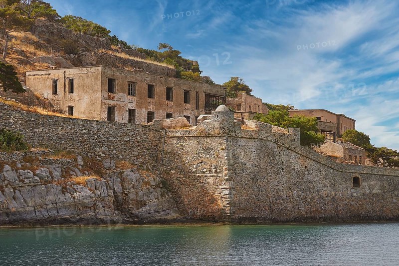 Dilapidated-looking old buildings on a rocky coastline surrounded by clear skies and calm seas, Venetian Sea Fortress, Leper Island, Spinalonga, Elounda Bay, Mirabello Bay, East Crete, Crete, Greek Islands, Greece, Europe