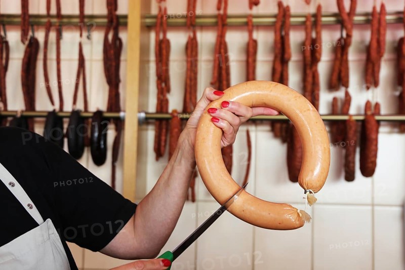 Saleswoman in the butcher's shop holds a knife to a sausage
