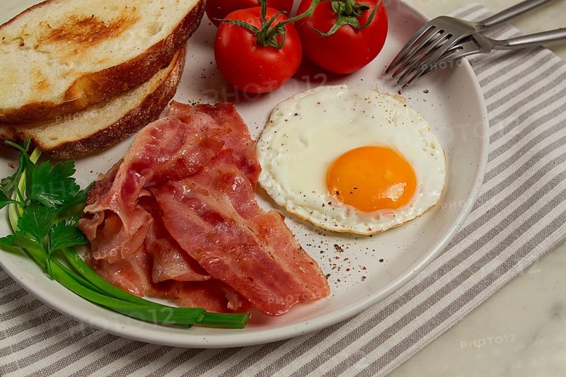 Breakfast, fried egg, bacon and bread, with cherry, on a light background, homemade, no people