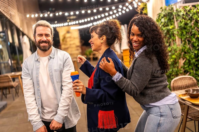 Multi-ethnic happy friends dancing while singing karaoke in the terrace of a bar