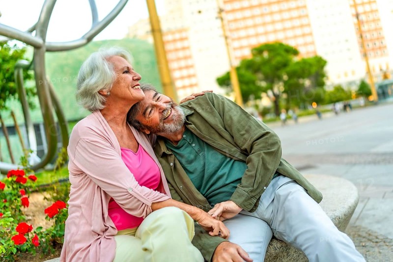 Mature couple sitting together in an urban bench contemplating the city views from the square
