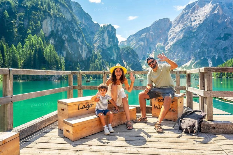 Happy family waving at lake braies, also known as pragser wildsee, enjoying summer vacation amidst the stunning scenery of the dolomites in italy