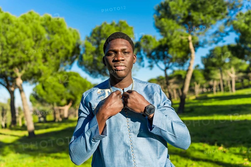 Young senegalese man wearing traditional dashiki attire, posing in a serene park setting, showcasing cultural pride and timeless fashion