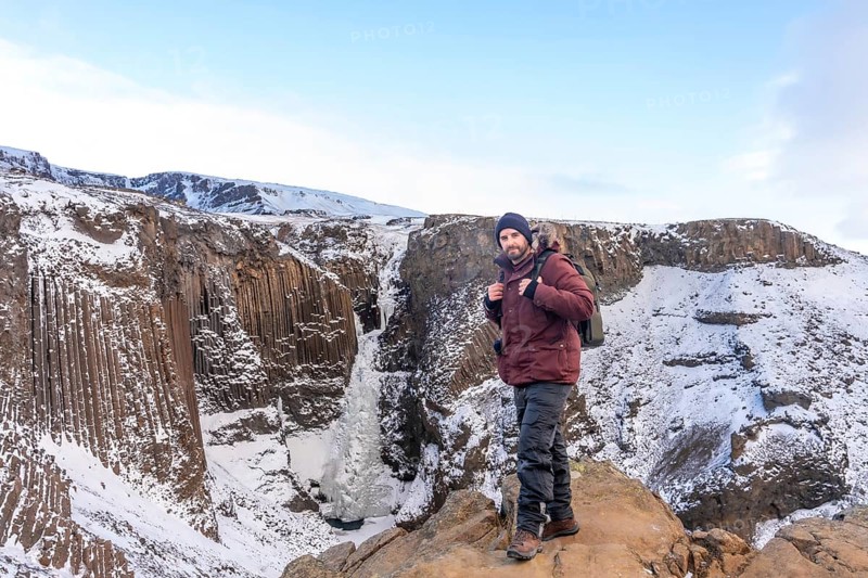 Portrait of a hiker at frozen Hengifoss waterfall in cold Iceland winter, volcanic cliffs