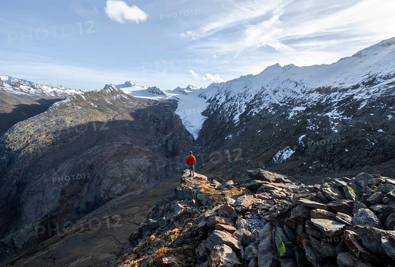 Mountaineer standing on a rock, surrounded by an impressive mountain landscape with snow-covered peaks in autumn View of Gurgler Ferner with summit Hochwilde and Falschungsspitze, Ötztal Alps, Tyrol, Austria, Europe