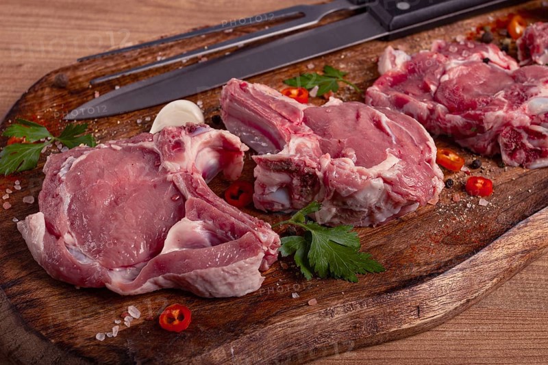 Raw calf meat, meat on the bone, meat for barbecue, cutting board, with spices and herbs, top view