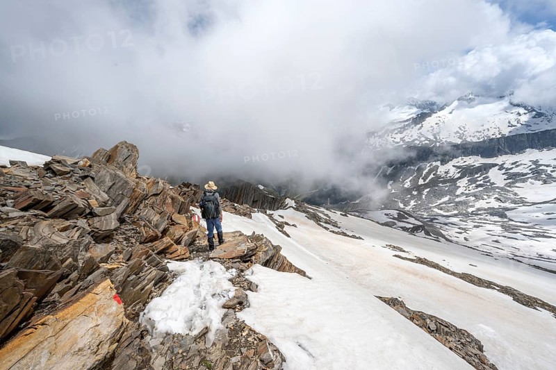 Mountaineer on a rocky ridge with snow, descent from the summit of Schönbichler Horn, view of snow-covered mountain peaks and valley Zemmgrund, Berliner Höhenweg, Zillertal Alps, Tyrol, Austria, Europe