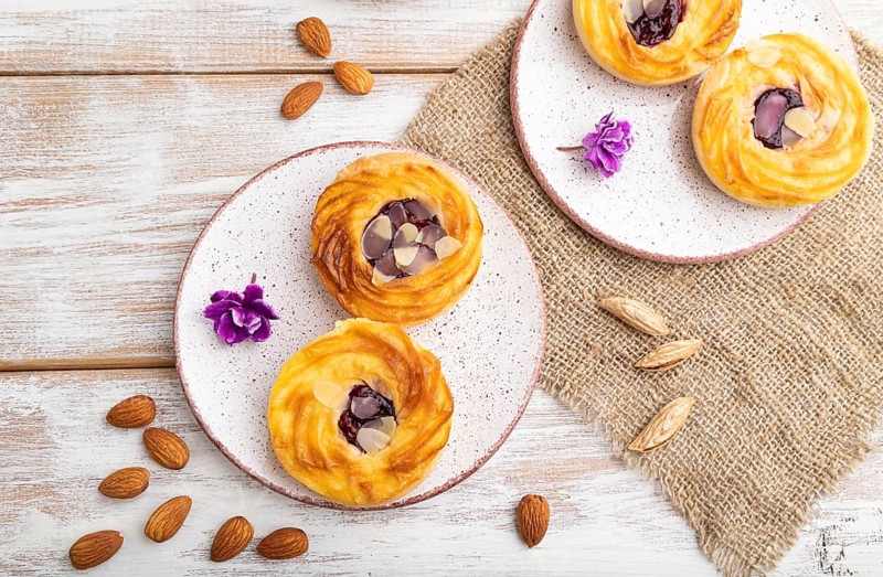 Small cheesecakes with jam and almonds with cup of coffee on a white wooden background and linen textile. top view, flat lay, close up