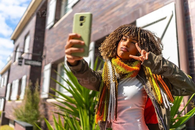 Beauty latin woman gesturing victory while taking a selfie standing next to a house