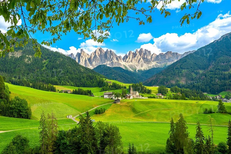 Framing the iconic santa maddalena church, green meadows and trees highlight the breathtaking summer scene in val di funes, with the majestic odle mountain range in the background