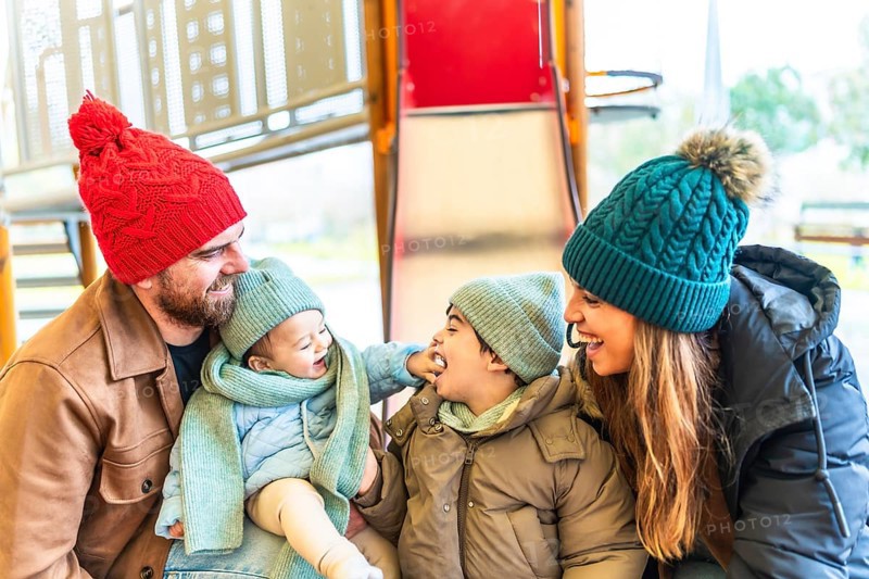 Happy family wearing winter clothes is having fun at the playground, enjoying precious moments together