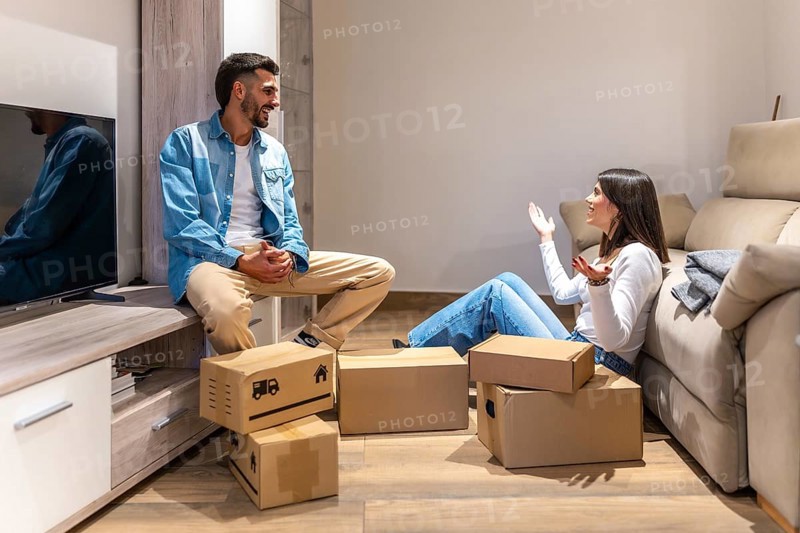 Young couple talking and smiling while unpacking cardboard boxes in new home, planning the arrangement of furniture