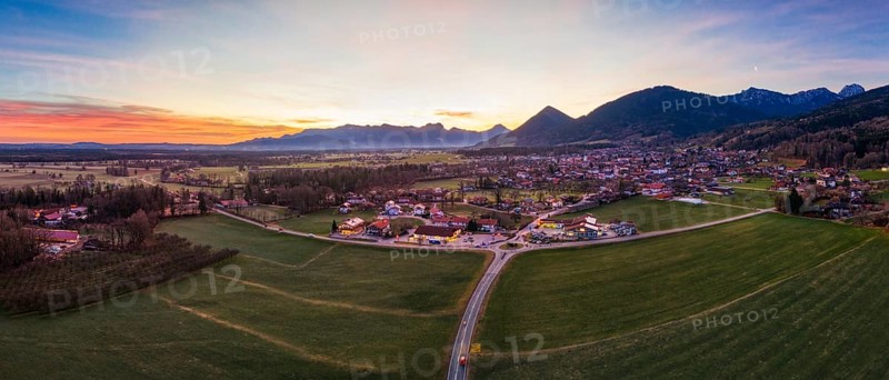 Panoramic view of a village in a wide green plain with mountains in the background at dusk, Bad Feilnbach