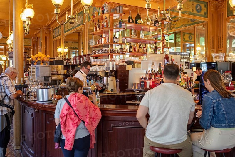 Cosy café with people at the counter, warm wood panelling and glowing lamps, Paris