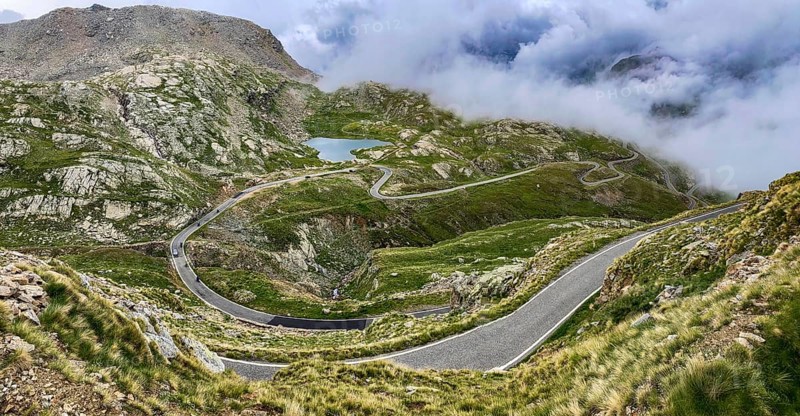 In the foreground a winding pass road to the Colle del Col de Nivolet pass, in the background a small lake naturally dammed by snowmelt, Gran Paradiso National Park, Ceresole Reale, Piedmont, Italy, Europe