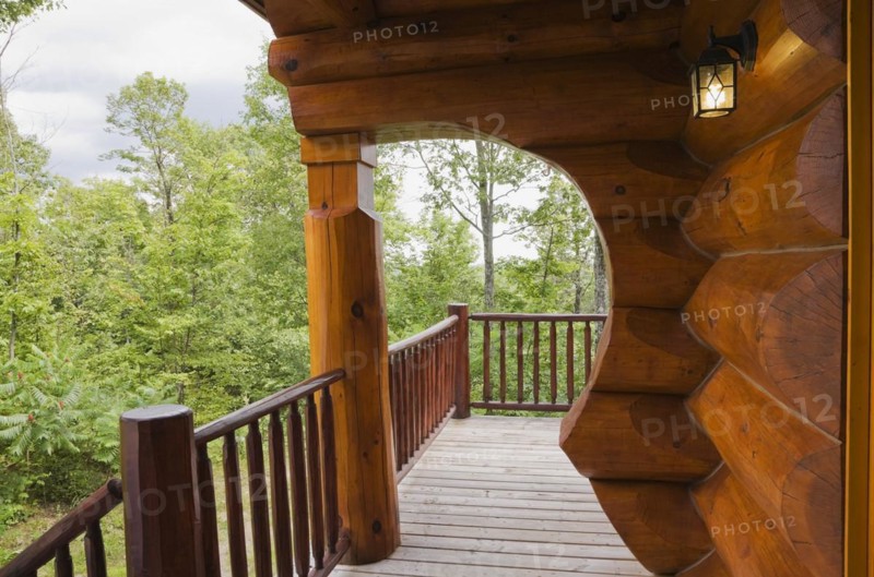Brown reddish stained Scandinavian log cabin home with with arch and wall made of large chinked logs and grey wood plank veranda in summer, Quebec, Canada, North America