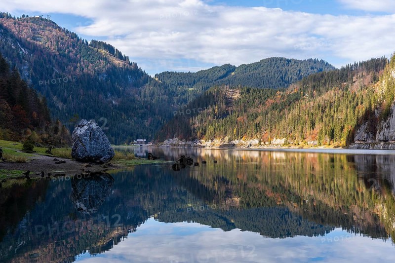 The Vordere Gosausee in autumn with a view of the Gasthof Gosausee. On the left a large rock on the lake shore, good weather, blue sky, clouds. Reflection. Top left the mountain station of the Gosaukammbahn cable car. Vorderer Gosausee, Gosau, Gosau valley, Salzkammergut, Upper Austria, Austria, Europe