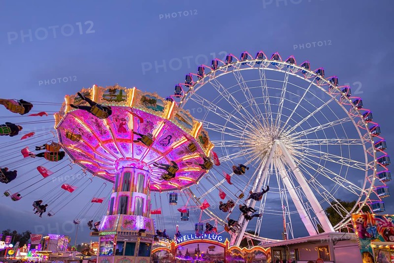 A lively funfair at dusk, illuminated by a large Ferris wheel and a colourful chain carousel, Cannstadter Volksfest, Stuttgart-Bad Cannstadt, Baden-Württemberg