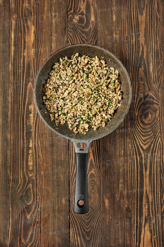 A skillet filled with sauteed diced mushrooms mixed with fresh herbs on a rustic wooden table. The dish showcases a blend of champignons and greens, ready for serving