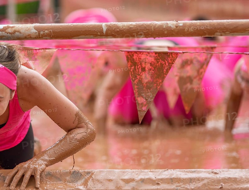 Participant climbs through muddy obstacles in a sporting competition
