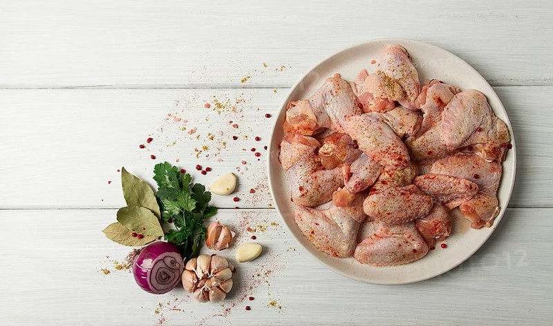 Frische, rohe Hähnchenflügel, mit Gewürzen, auf einem weißen Holztisch