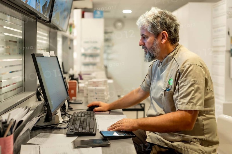 Side view portrait of a male mature pharmacist using computer for paperwork in the office